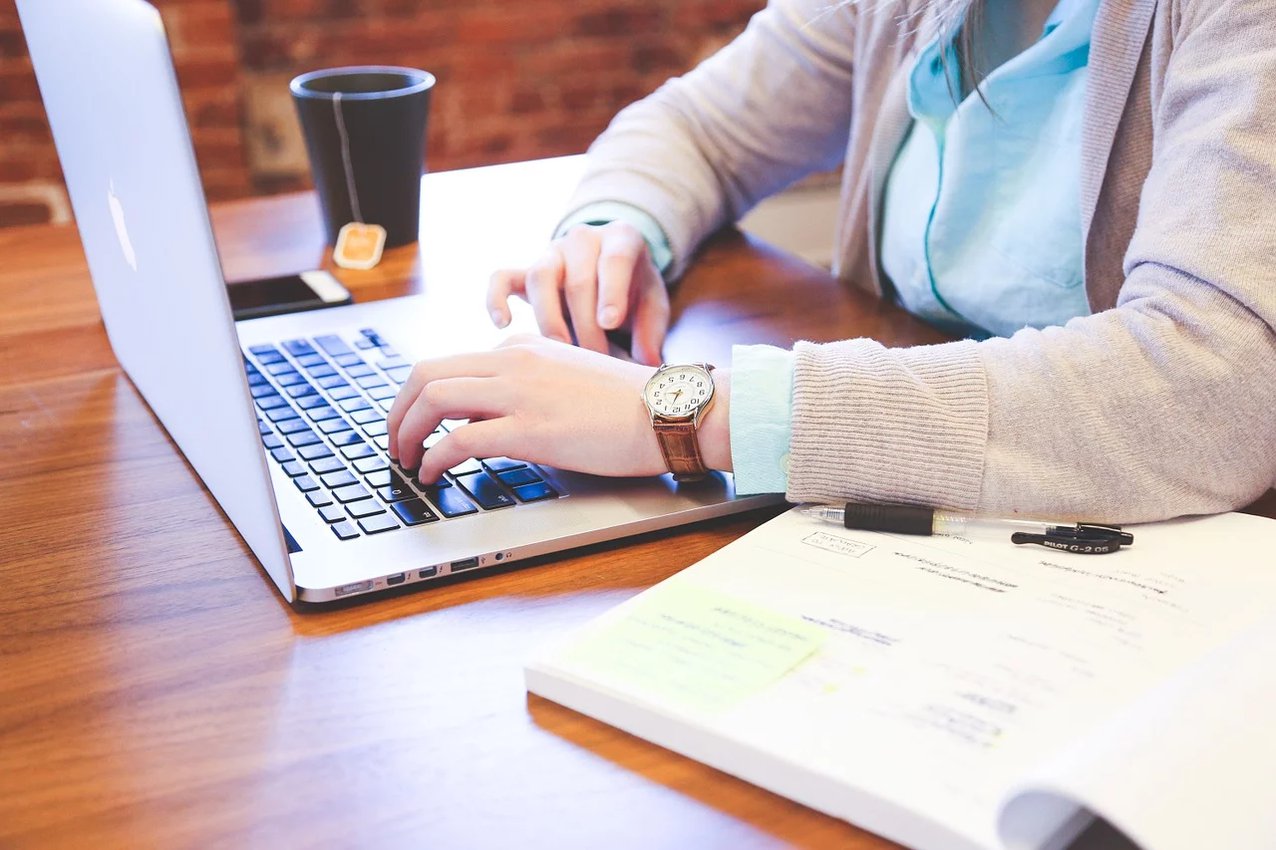 Person, die an einem Schreibtisch mit einem Laptop, einem Notebook und einer Tasse Kaffee arbeitet